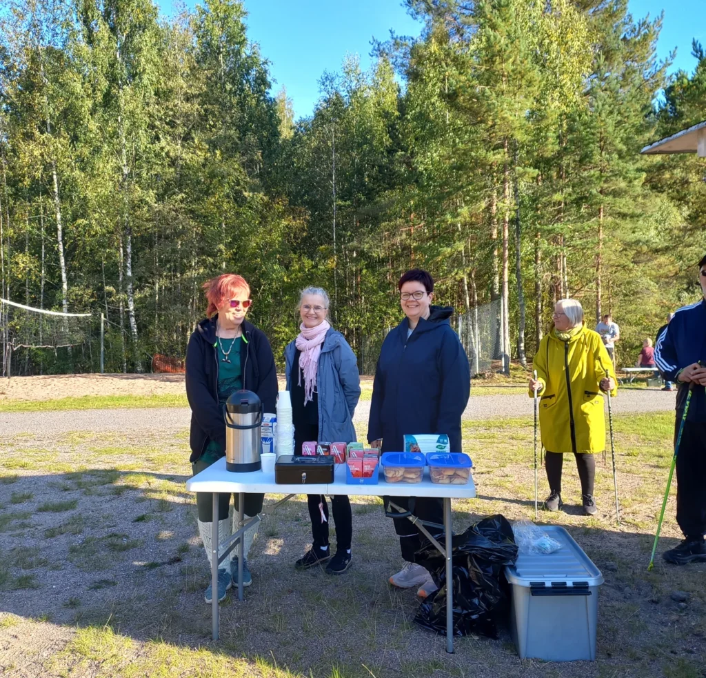 Kolme naista pitämässä kahviota, naisten edessä pöydällä kahvitermari, pillimehuja ja pullaa
