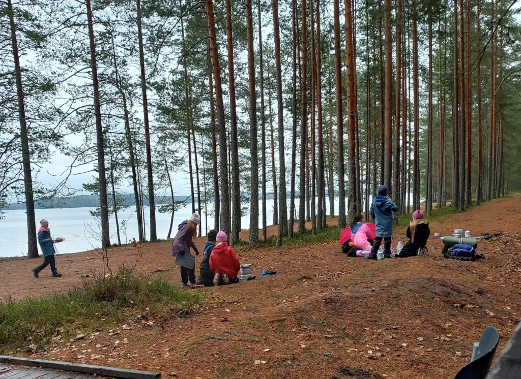 Partiolaisia metsäisellä rannalla tekemässä ruokaa