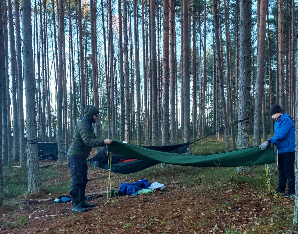 Kaksi partiolaista viikkaa tarppia metsässä